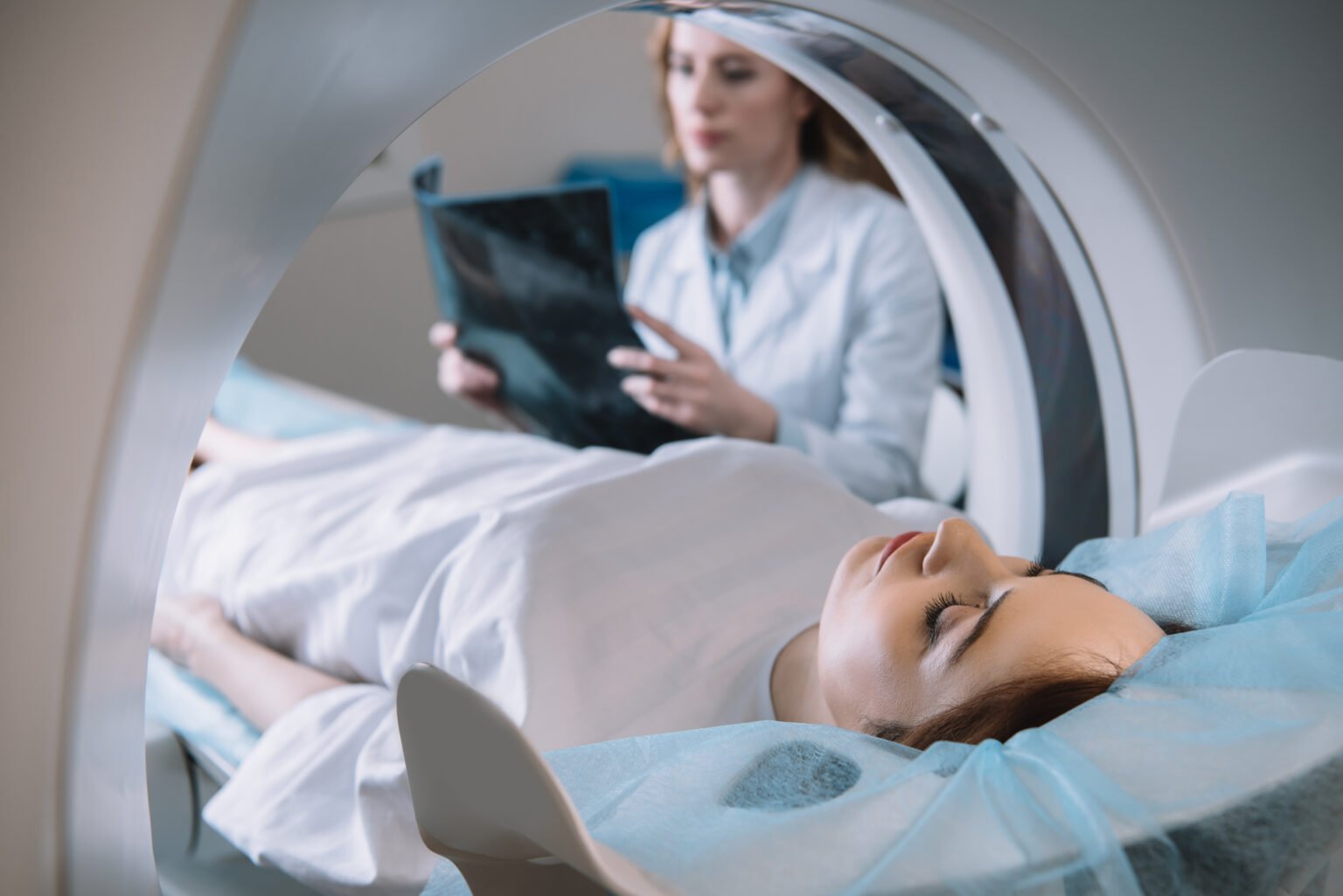 selective focus of radiologist holding x ray diagnosis while patient lying on ct scanner bed during